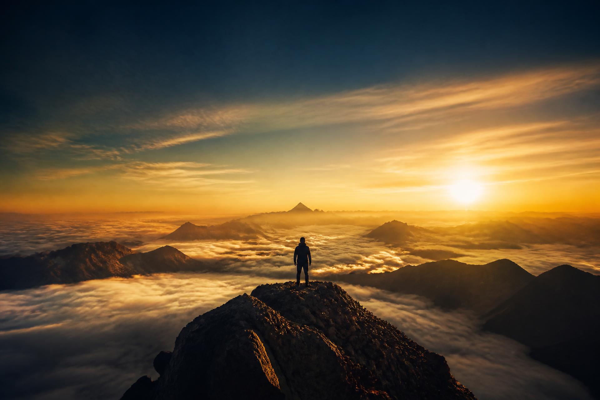 Silhueta de uma pessoa no topo da montanha ao nascer do sol